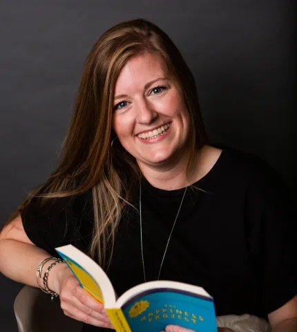 Shelby Cleary, Chief Administrative Officer at Holmes & Palmer Orthodontics, smiling while reading a book, showcasing a friendly and approachable demeanor.