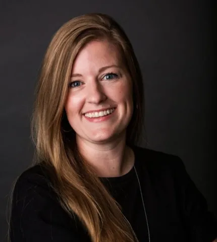 Shelby Cleary, Chief Administrative Officer at Holmes & Palmer Orthodontics, smiling with long hair against a dark background, reflecting the team's friendly and professional atmosphere.