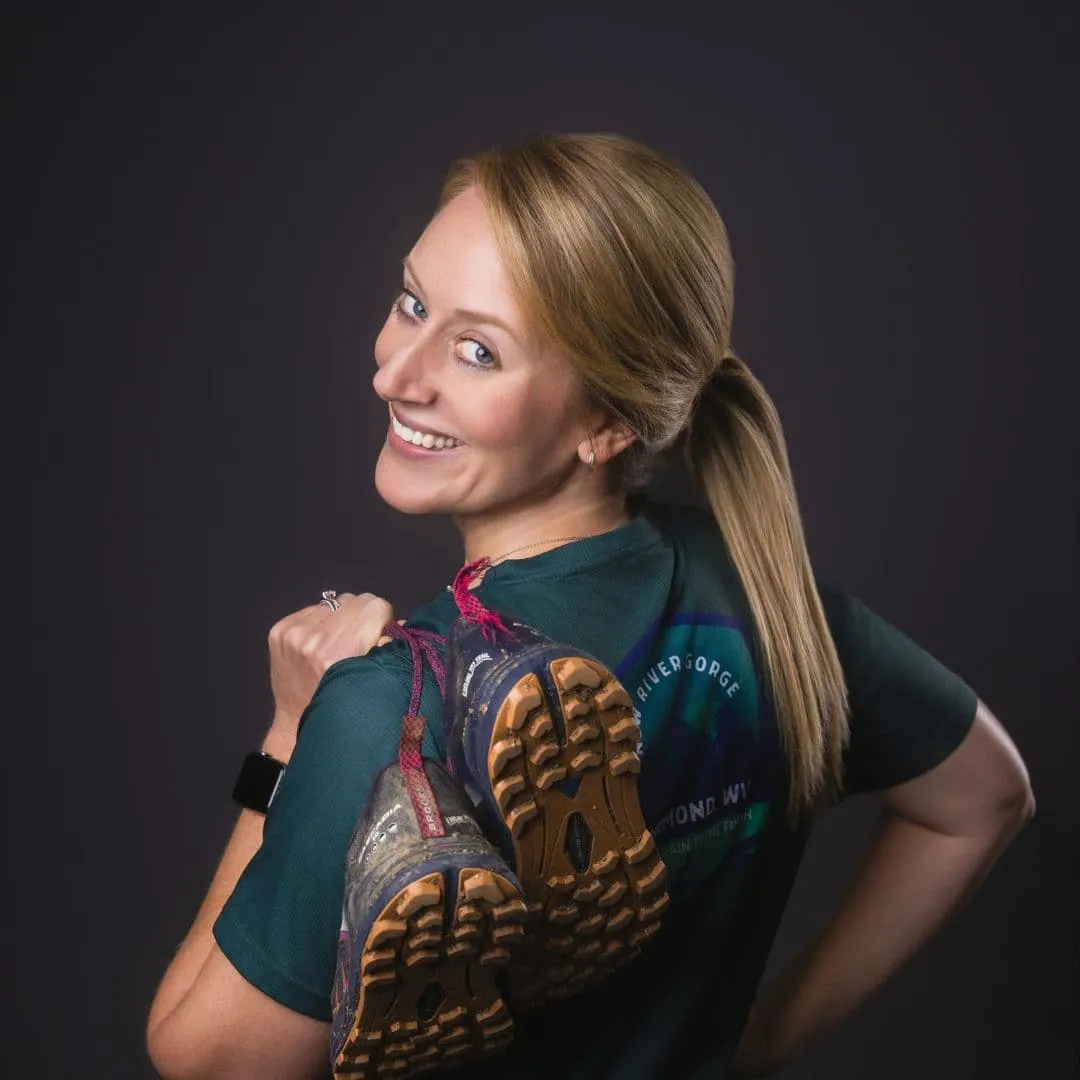 Smiling woman holding climbing shoes over her shoulder, showcasing her adventurous spirit, representing the friendly team at Holmes & Palmer Orthodontics.