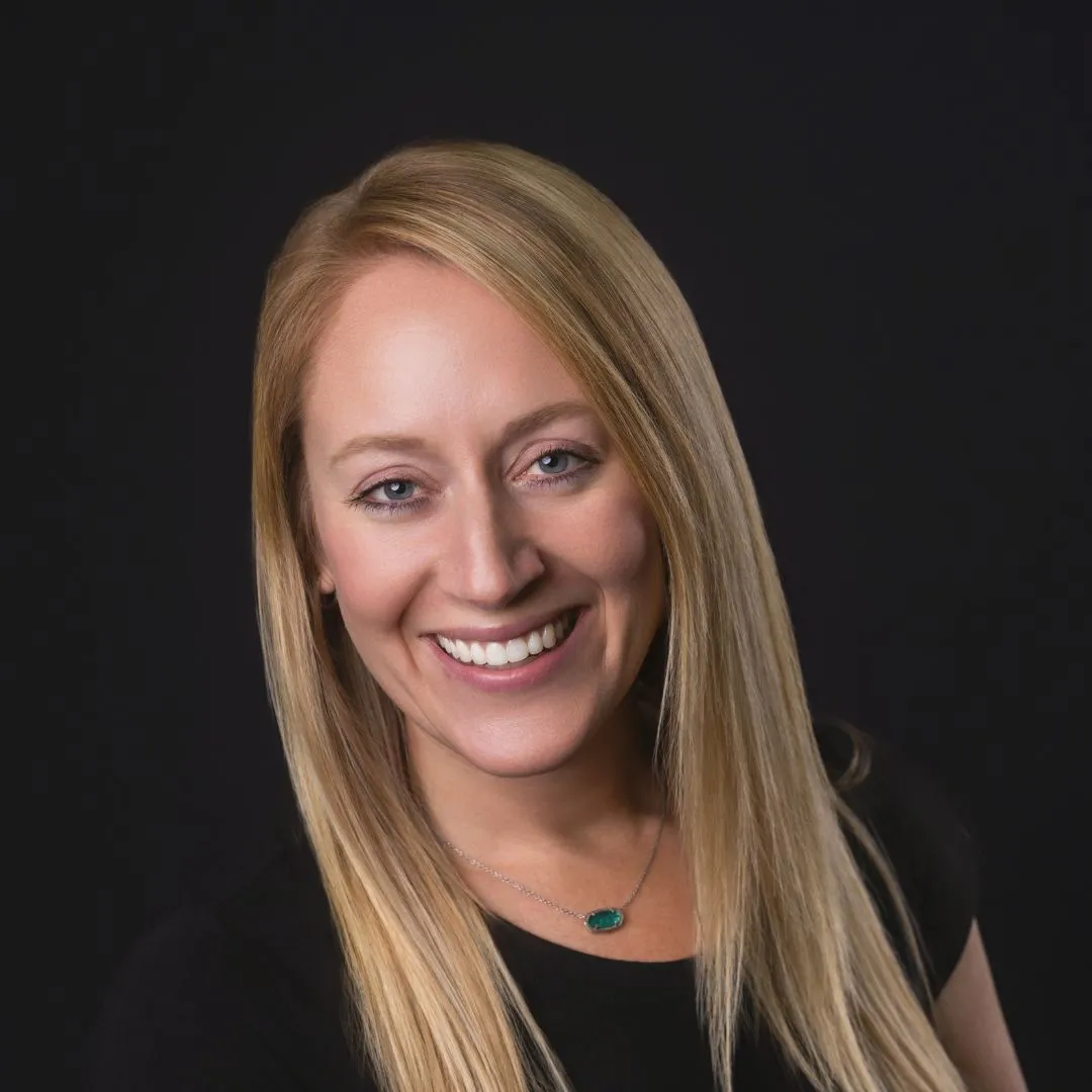 Smiling woman with long blonde hair wearing a black shirt and a necklace, representing the caring team at Holmes & Palmer Orthodontics.